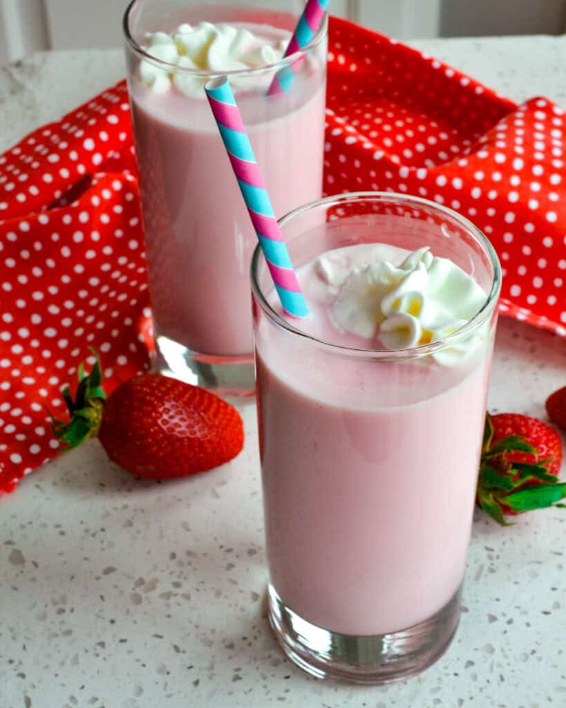 Strawberry Milk in glasses with a straw and whipped cream.