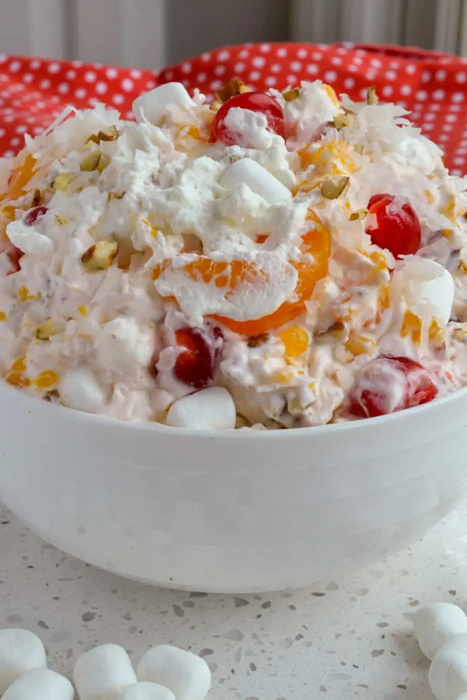 A bowl full of fruit, pecans, coconut, marshmallows, and whipped cream mixed together. 