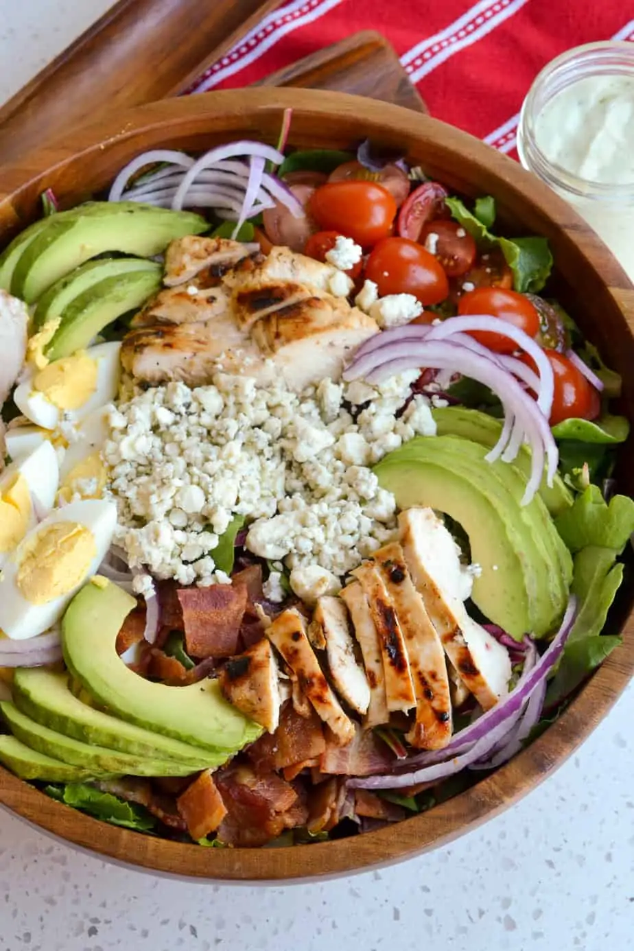 A salad bowl filled with greens, chicken, bacon, tomatoes, eggs, and avocado. 