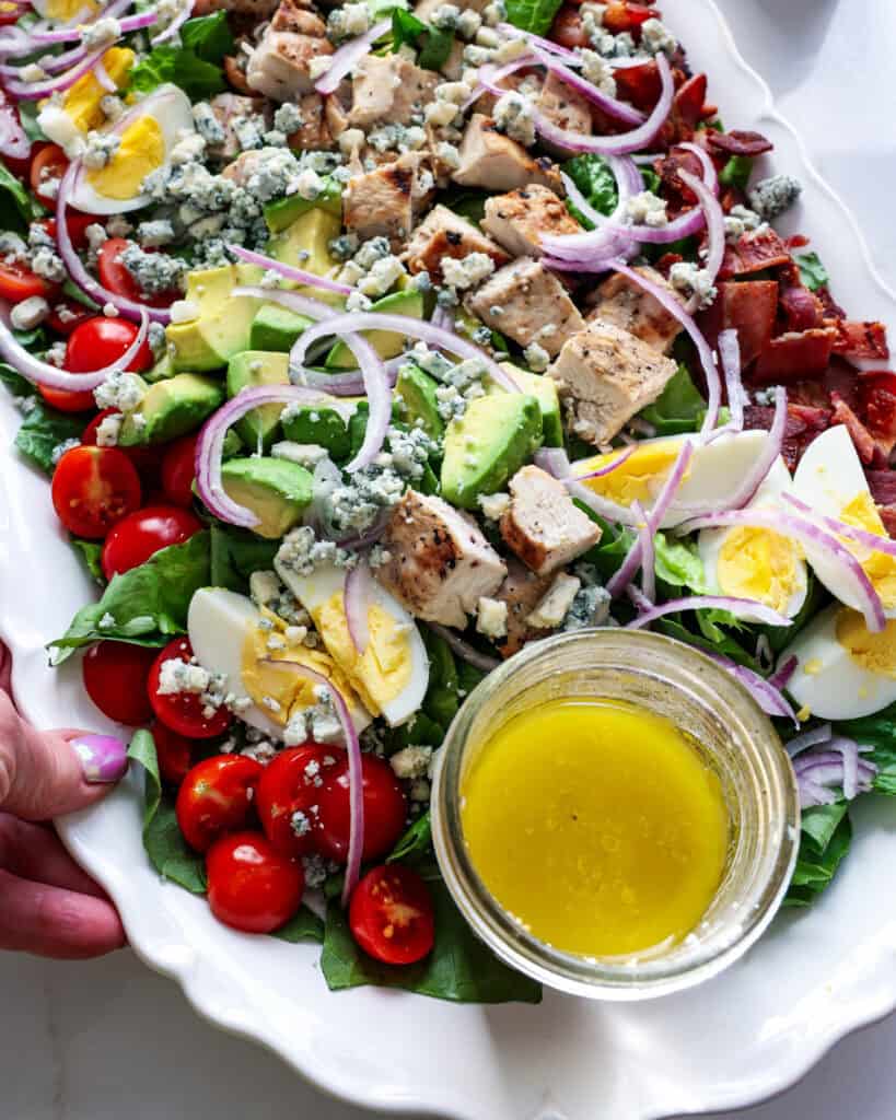 A close up view of cobb salad with grilled chicken, bacon, hardboiled egg, diced avocado, red onion, and crisp bacon.