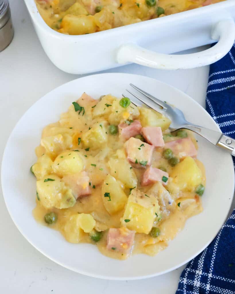 Cheesy ham and potato casserole on a single serving plate with a fork on the side.