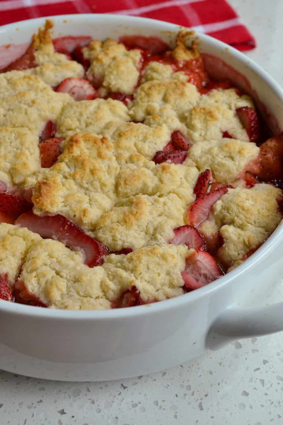 A casserole full of baked strawberries with a flaky biscuit topping. 