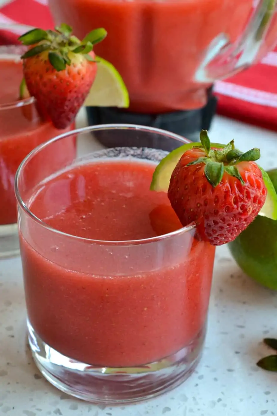A glass full of strawberry daiquiri garnished with a strawberry and lime slice. 
