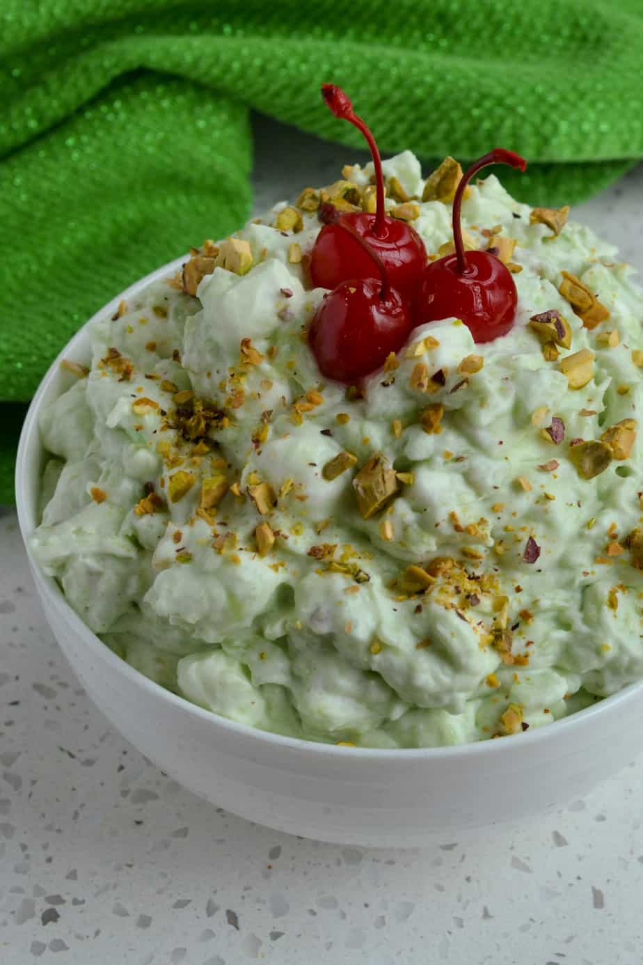 A bowl full of pistachio fluff and garnished with pistachios and maraschino cherries. 