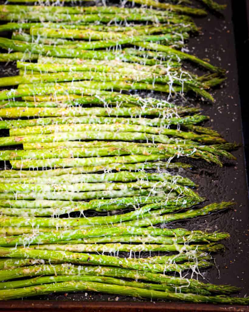 A baking sheet full of air fried asparagus with lemon pepper and parmesan cheese. 