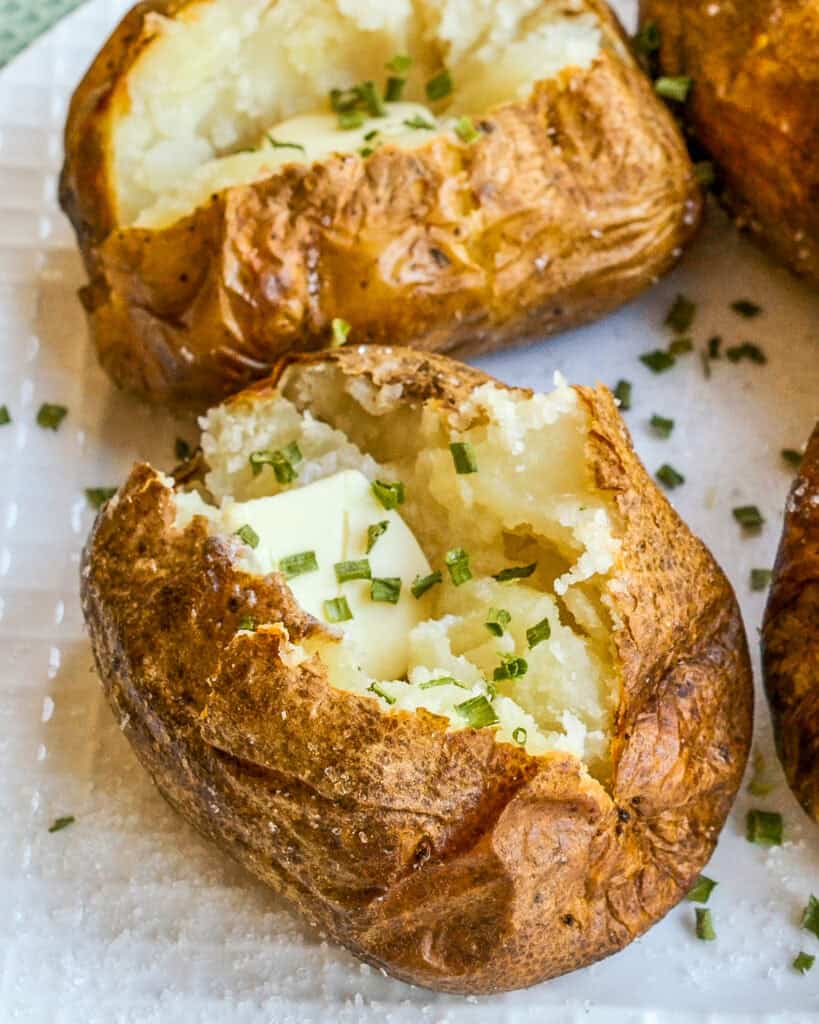 Potato air fried served on a plate with chives and butter on top.