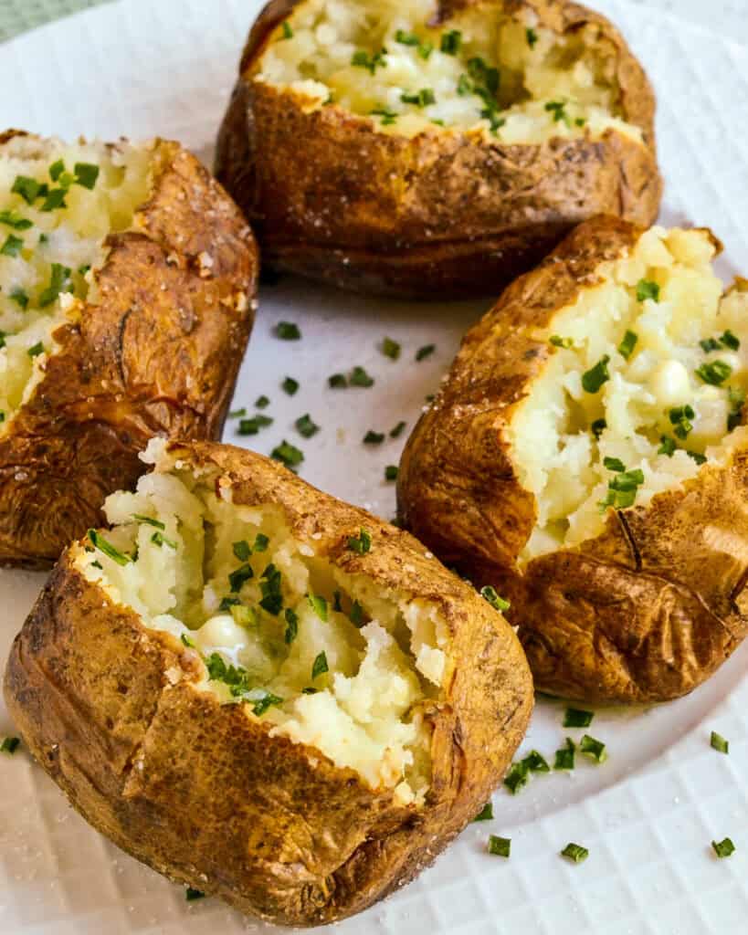 All four potatoes air fried served on a plate with chives and butter on top.