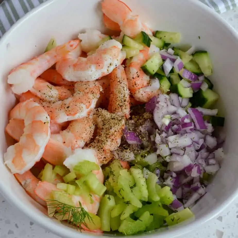 Cooked shrimp, chopped celery, chopped cucumber and chopped red onion in a bowl. 
