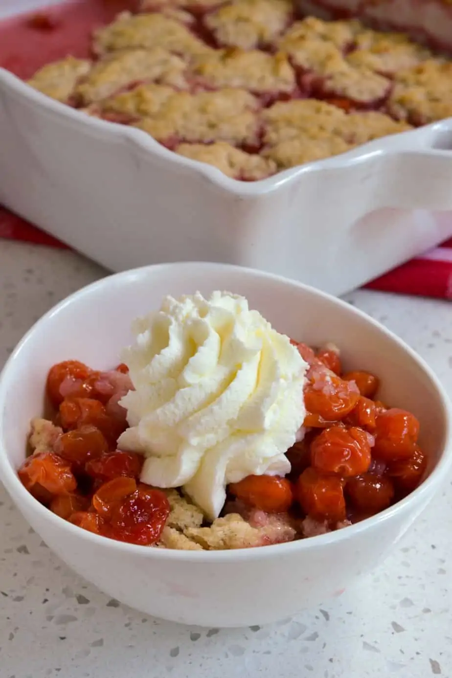 A bowl of cherry cobbler topped with whipped cream. 