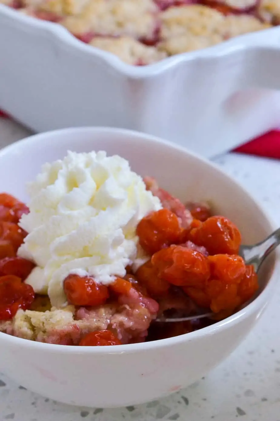 An individual serving of fresh cherry cobbler topped with homemade whipped cream. 
