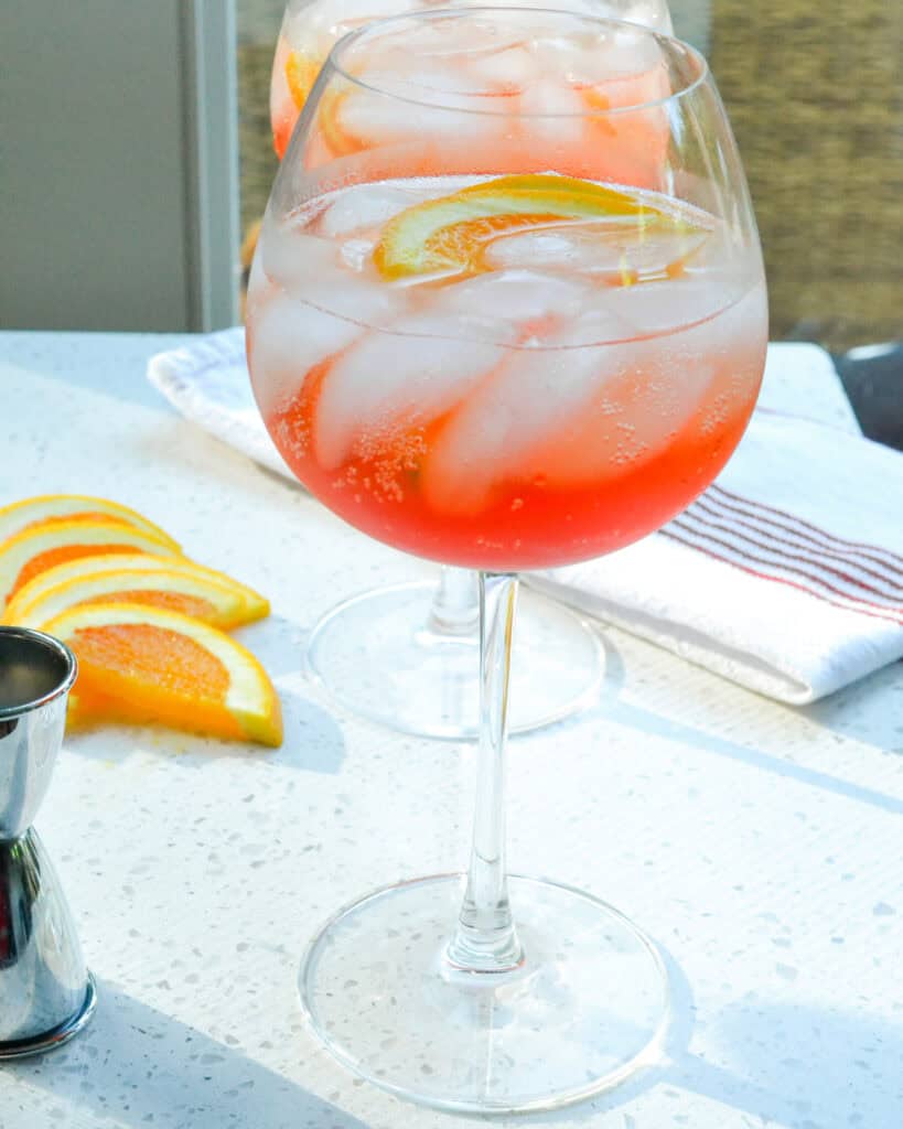 Two glasses full of aperol spritz with orange slices and a bar towel in the background. 