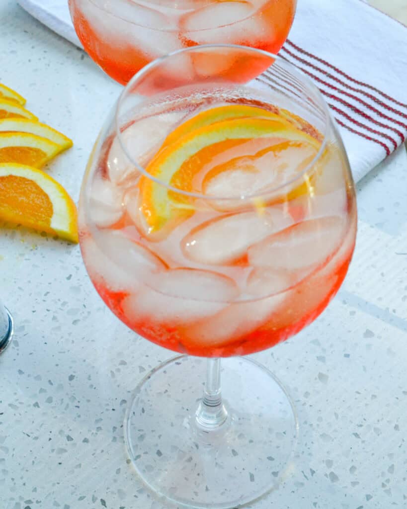 Two big bowl wine glasses full of aperol spritz and garnished with orange slices. 