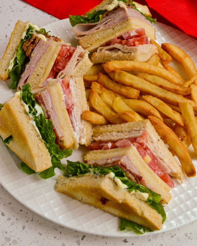 A quartered club sandwich on a white plate with French fries.