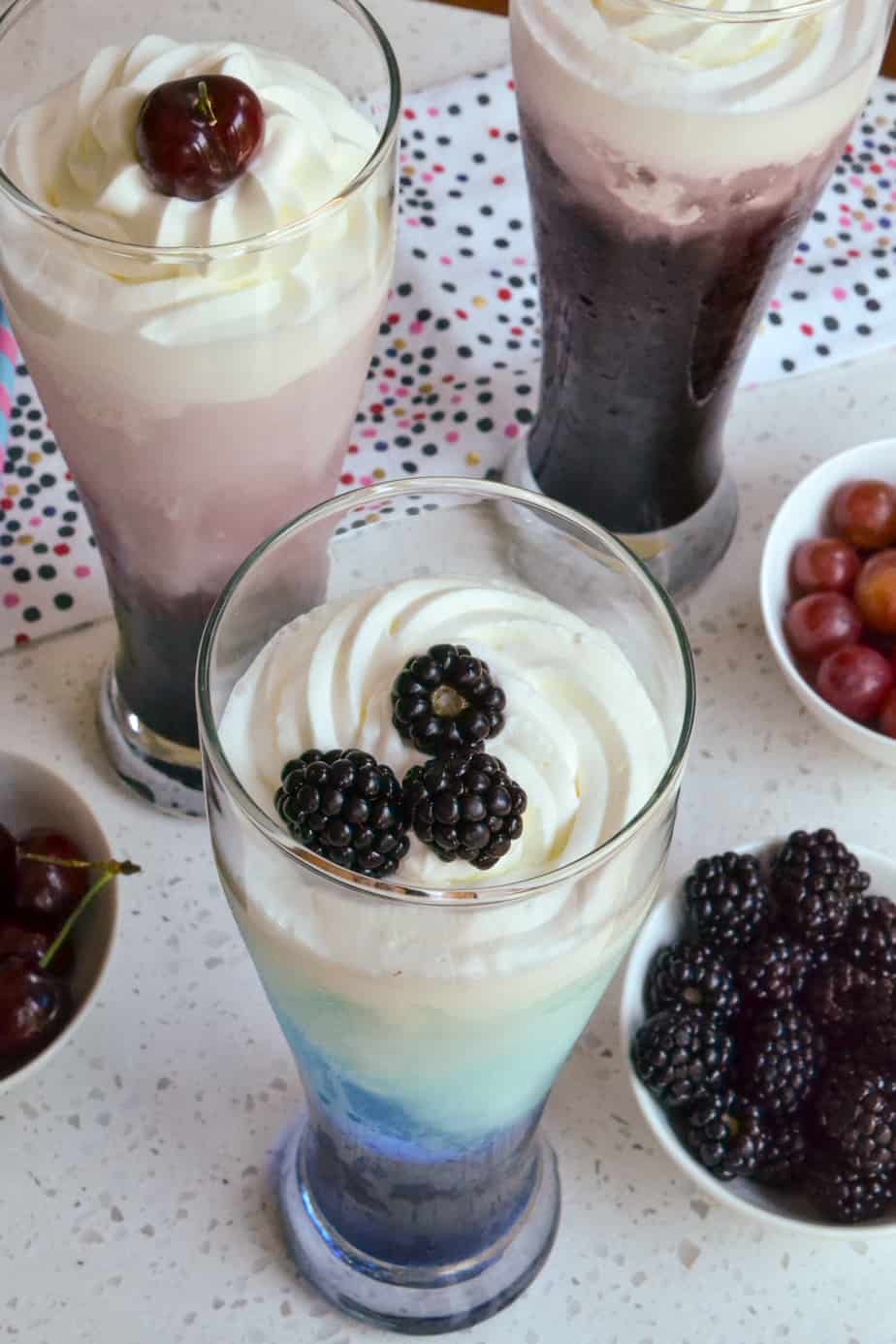 A blackberry Italian soda in a tall glass garnished with with whipped cream and fresh blackberries. 