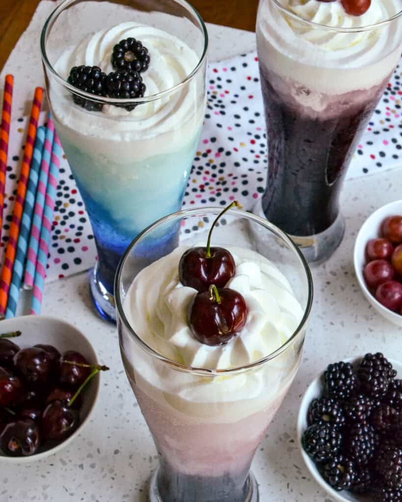 Cherry flavor Italian Cream Soda up close with fruit in bowls and two other flavor variations behind.