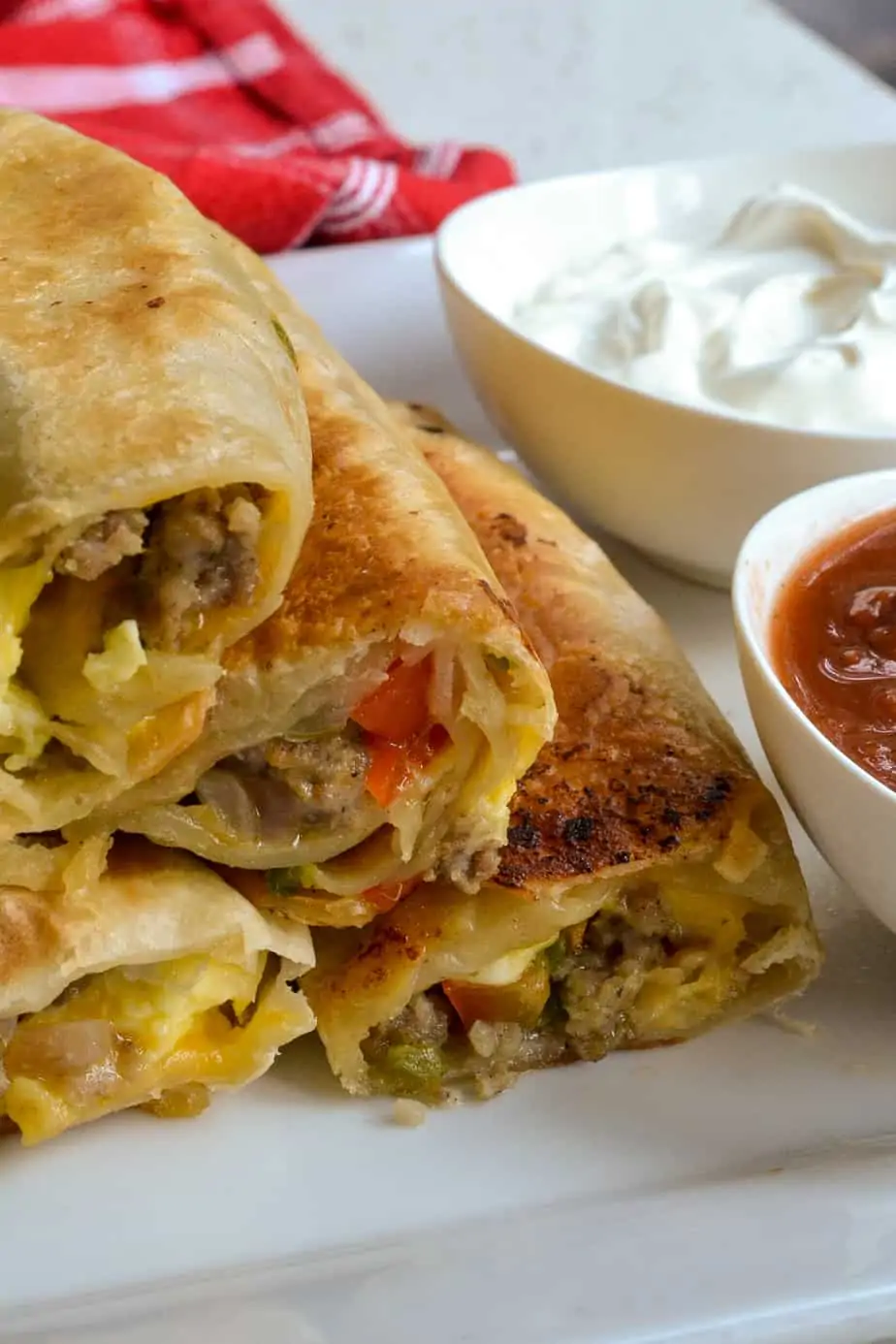 A plate full of breakfast burritos with salsa and sour cream. 