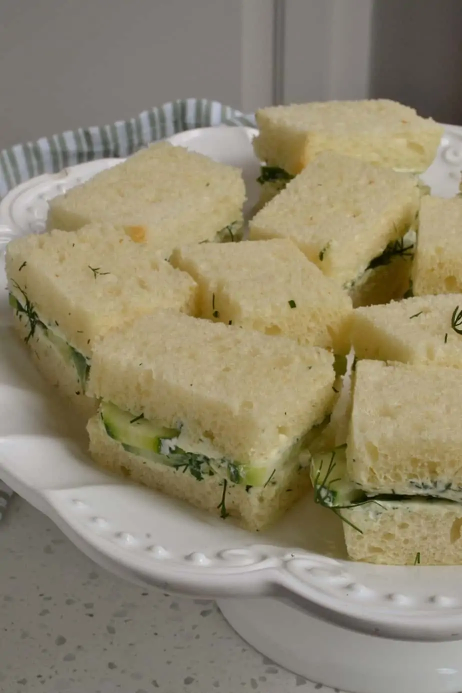 A white party platter with cucumber cream cheese sandwiches. 