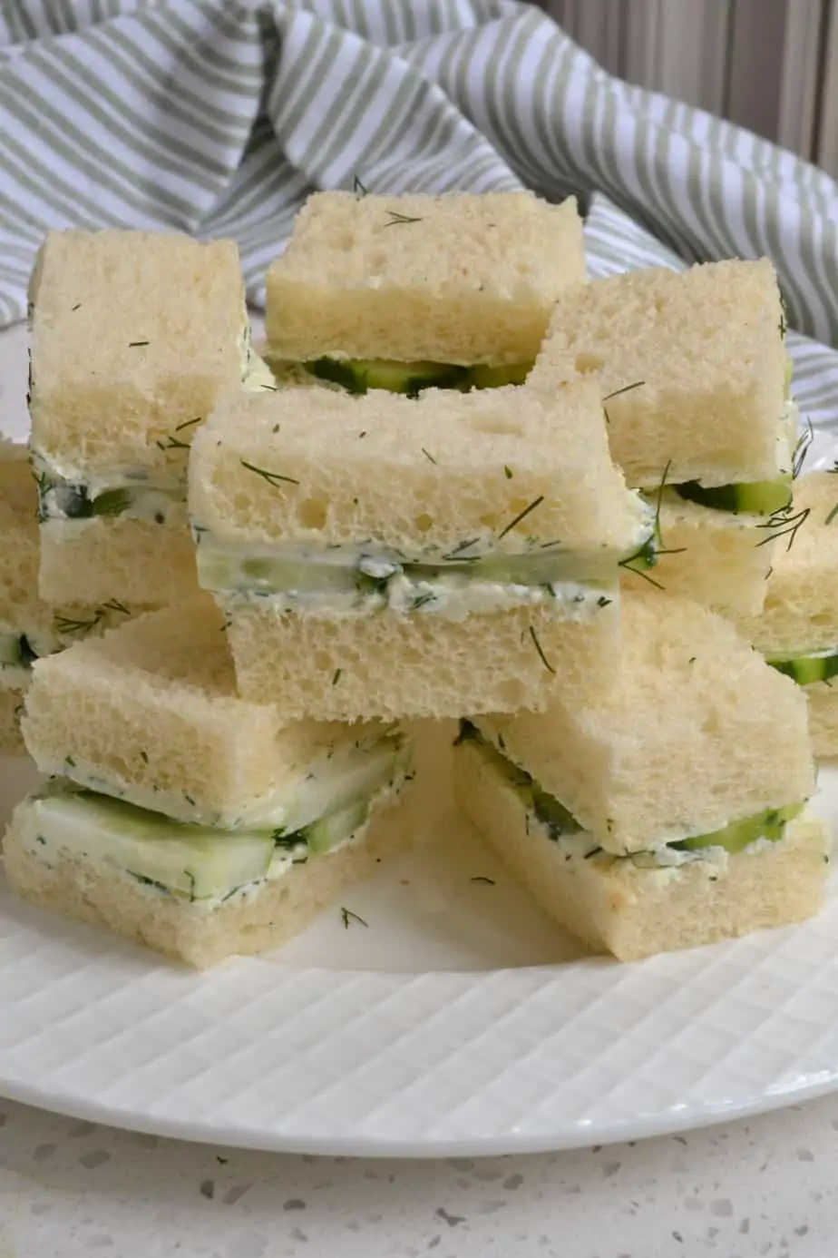 Cucumber tea sandwiches stacked on a plate. 