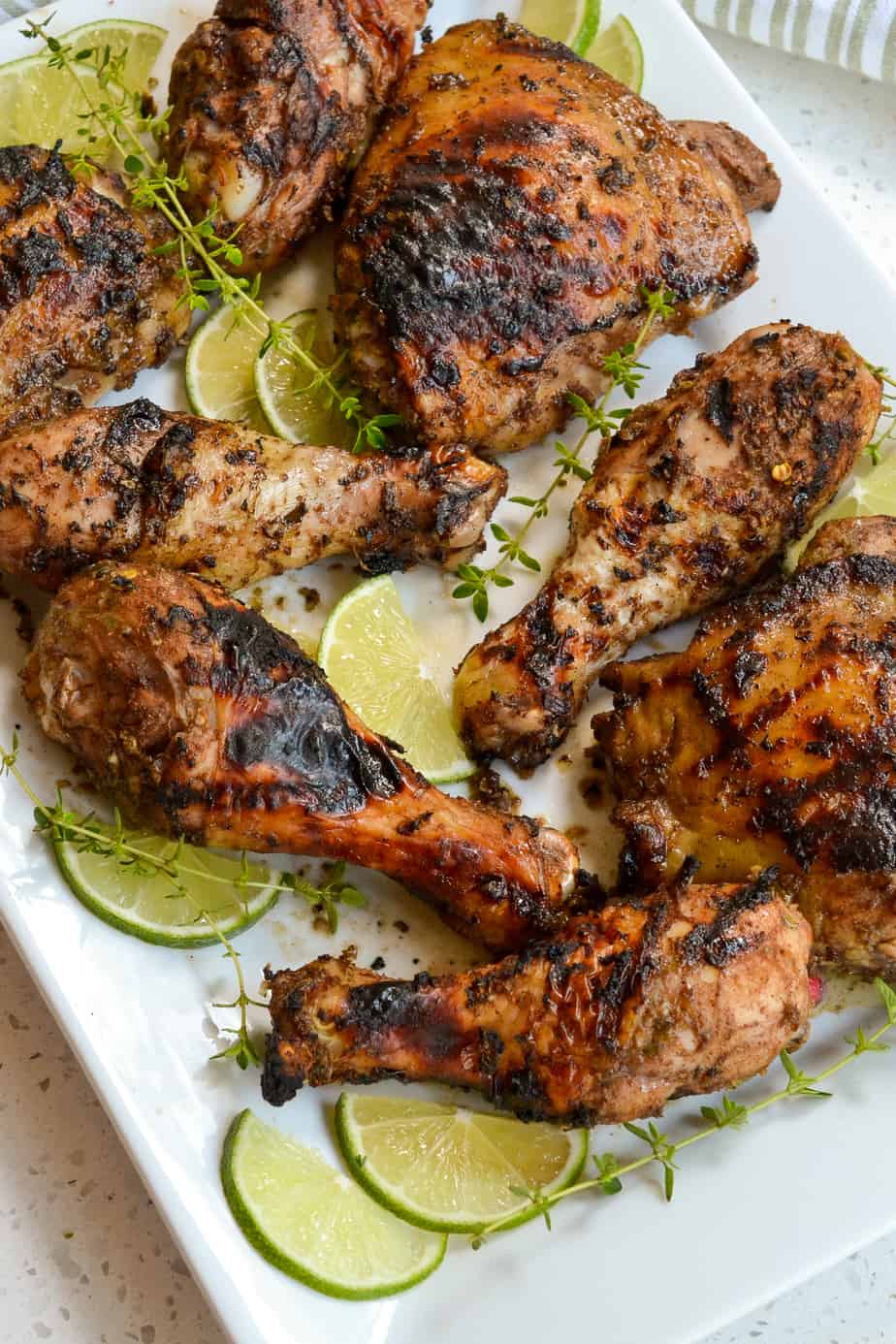 Jerk chicken legs and thighs on a platter with limes slices. 