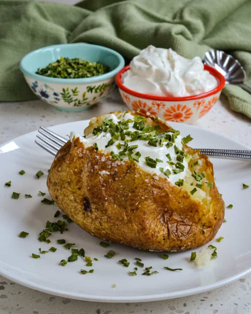 Oven Baked Potato served on a plate topped with sour cream and chives.
