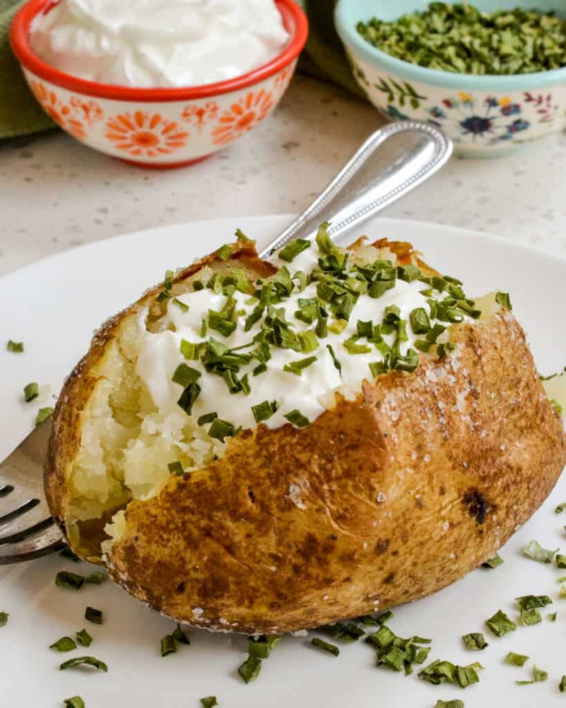 Oven Baked Potato served on a plate topped with sour cream and chives.