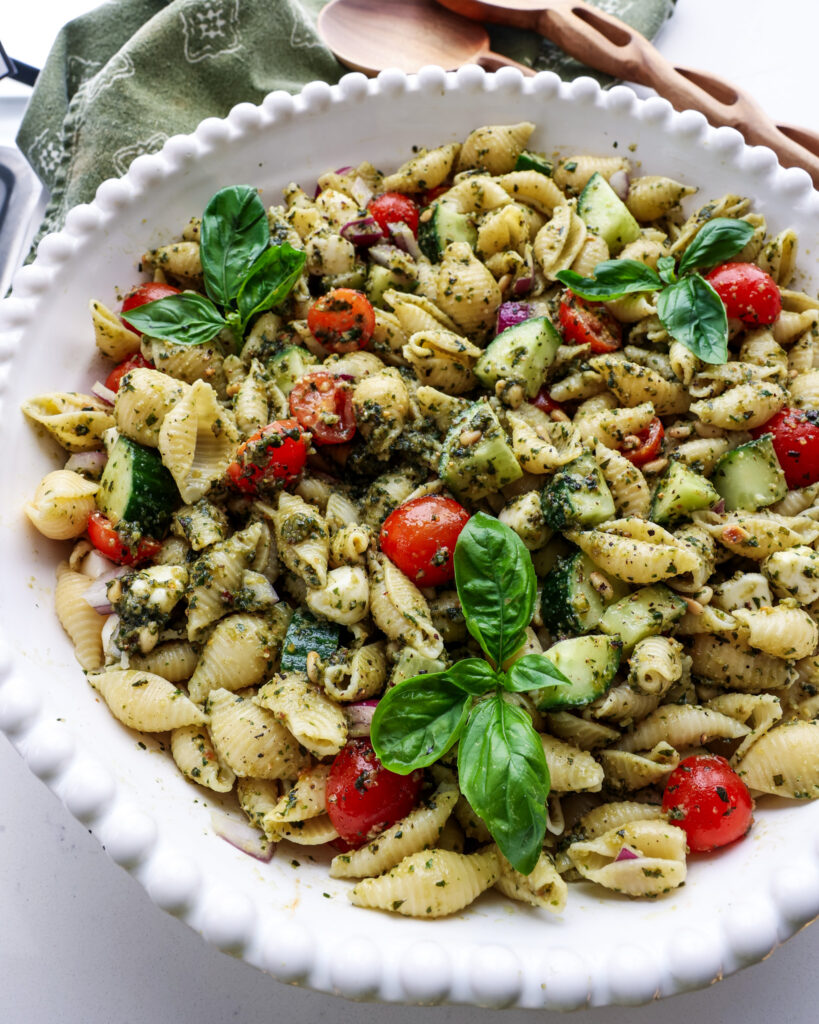 A very close view of pasta pasta salad in a large white serving bowl with tongs in the background. 