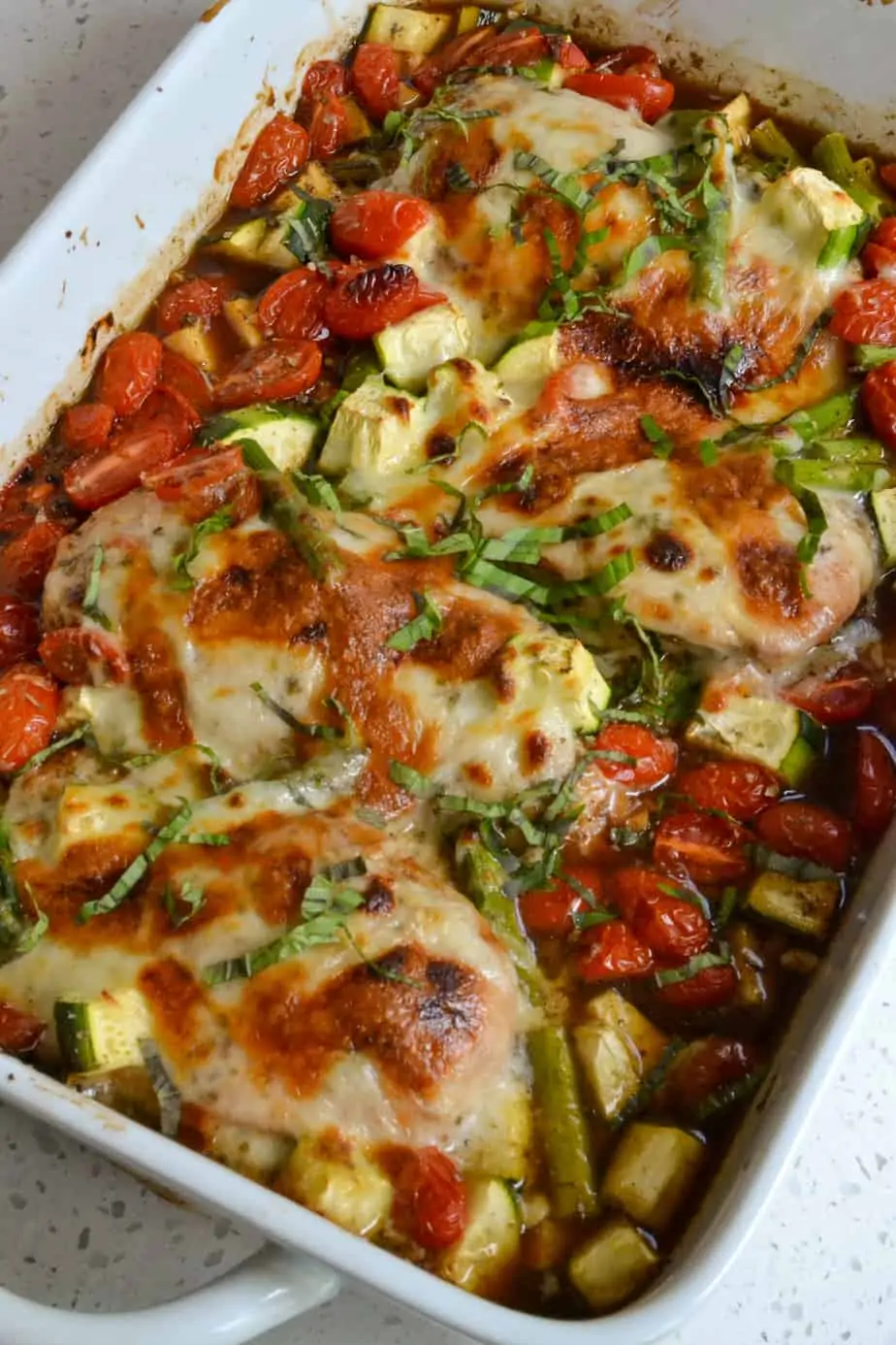 Casserole of baked chicken with tomatoes, asparagus, and zucchini topped with mozzarella. 