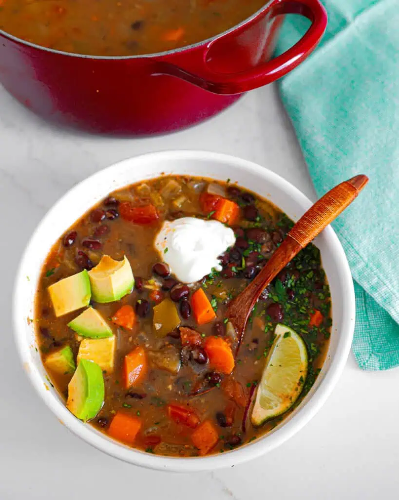A bowl of black bean soup topped with avocado, cilantro, sour cream, and limes.