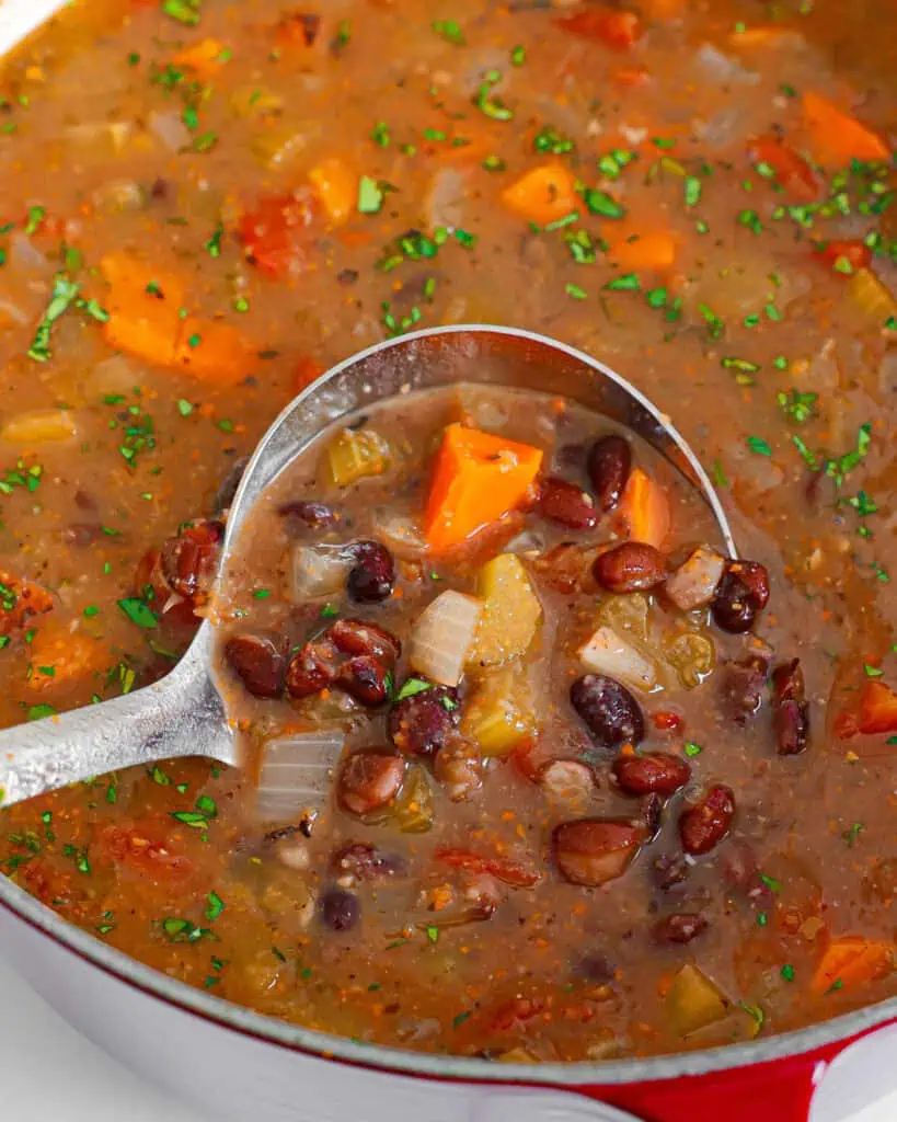 A close up view of a Dutch oven and a ladle full of black bean soup.