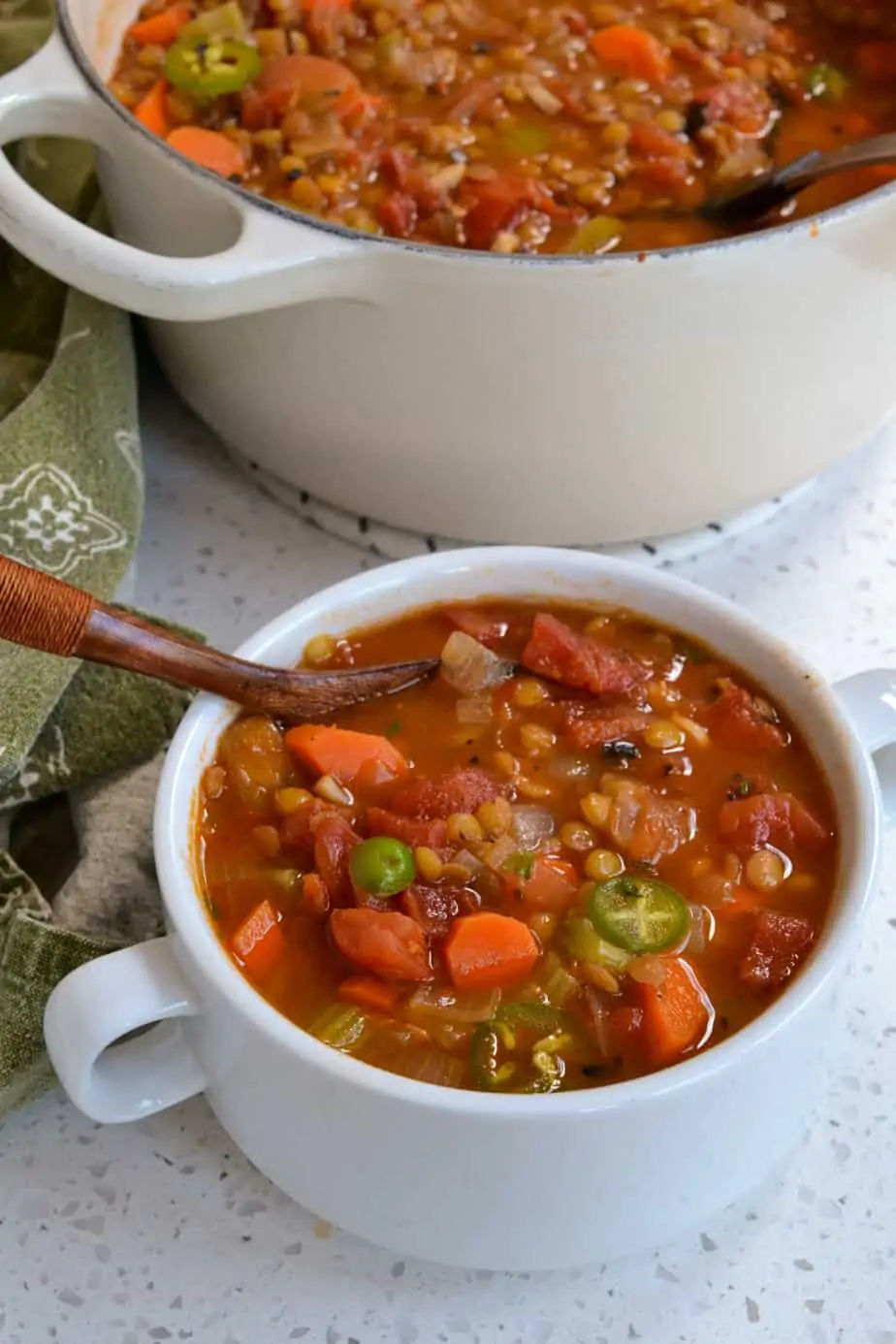 A bowl full of lentil vegetable soup topped with jalapeno rings. 