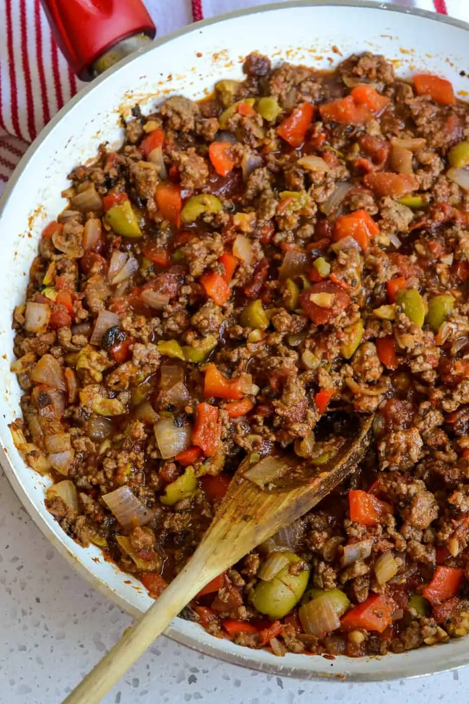 A skillet full of ground beef, tomatoes, tomato sauce, green olives, and chopped raisins. 
