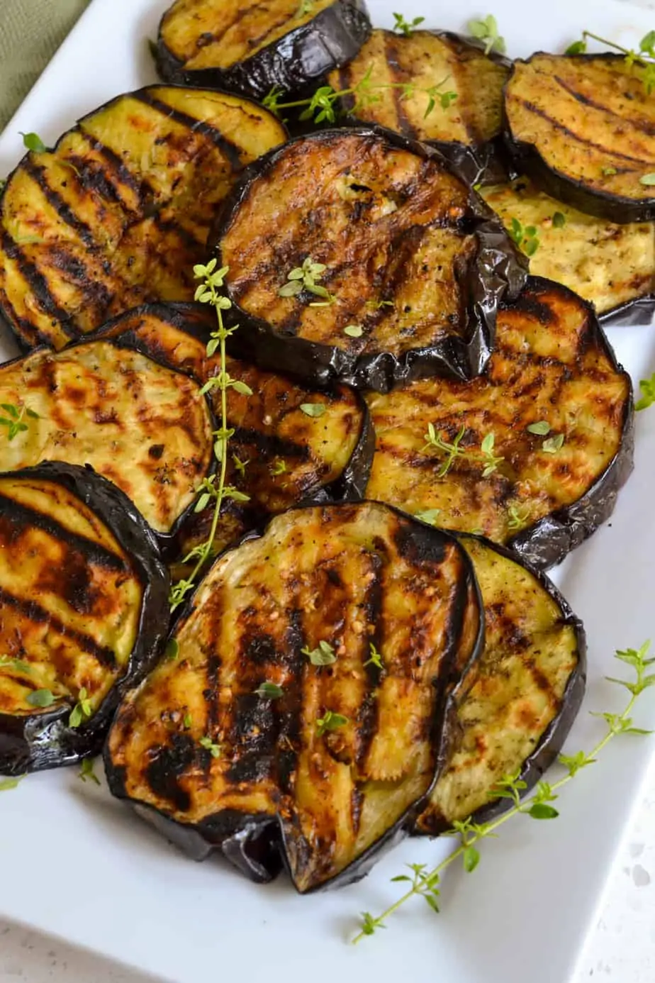 A platter full of grilled eggplant topped with fresh rosemary. 