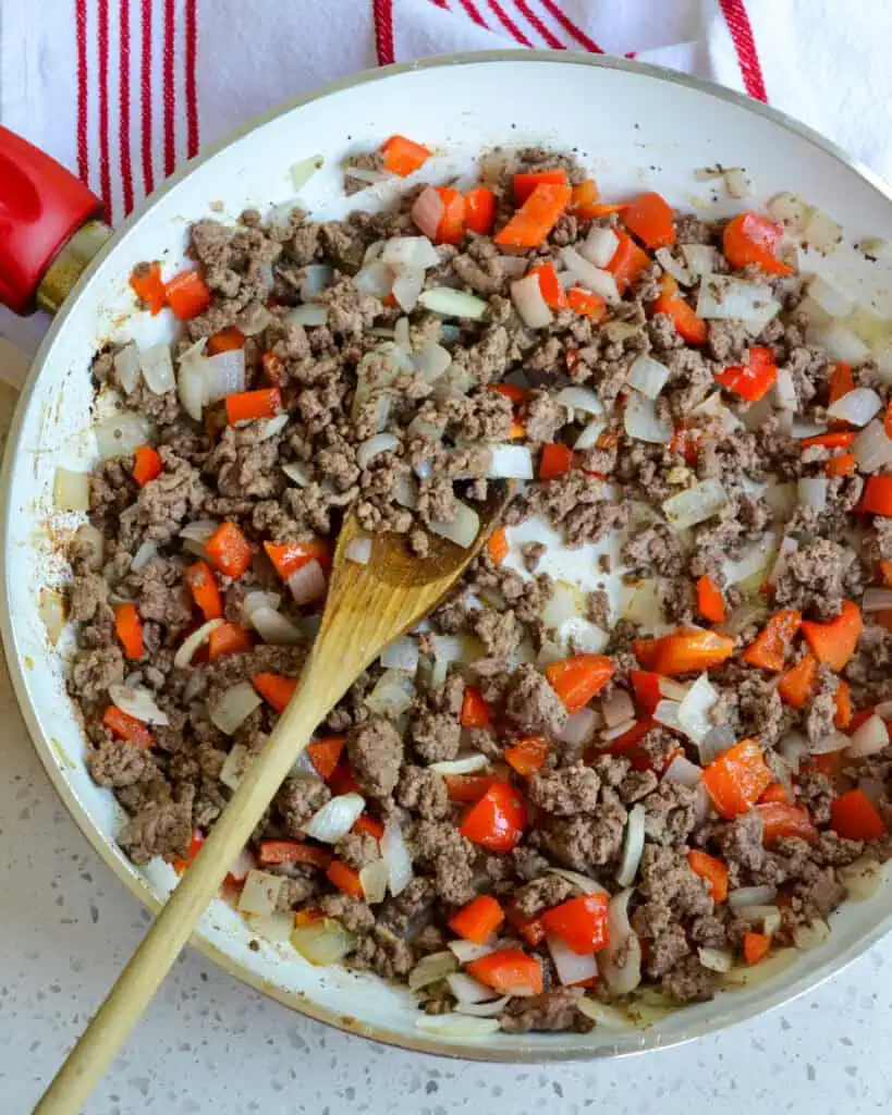 Start by browning the ground beef in a large skillet over medium-high heat. After it starts to brown for a couple of minutes, add the onion. Let it cook for a few minutes, then add the diced red bell pepper. Now cook until the vegetables are soft and the beef is browned. 