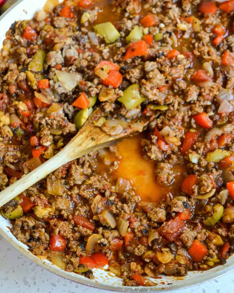A large white skillet full of Cuban picadillo with a wooden spoon in it.  