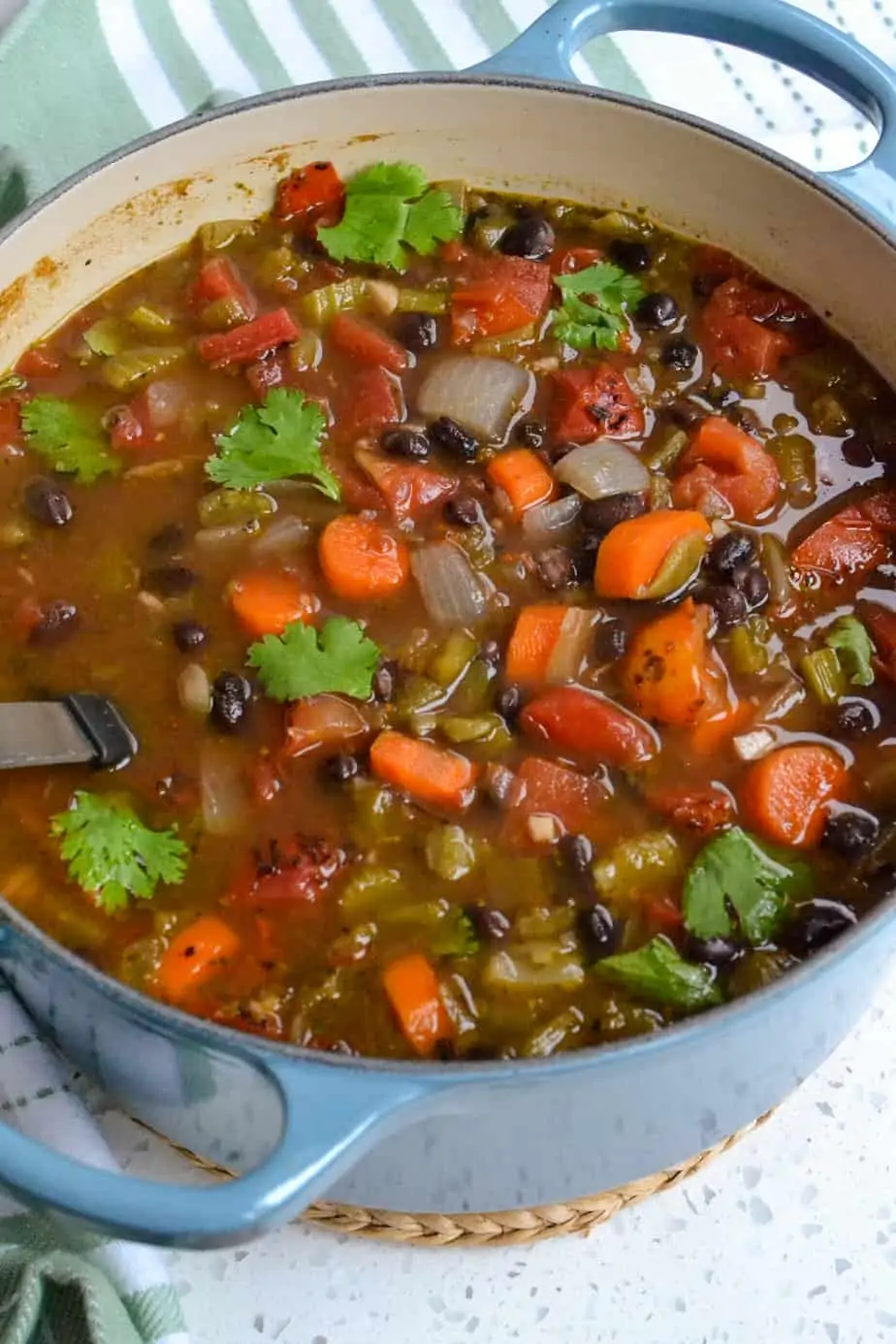 A Dutch oven full of black bean soup with carrots, tomatoes, and green chiles. 
