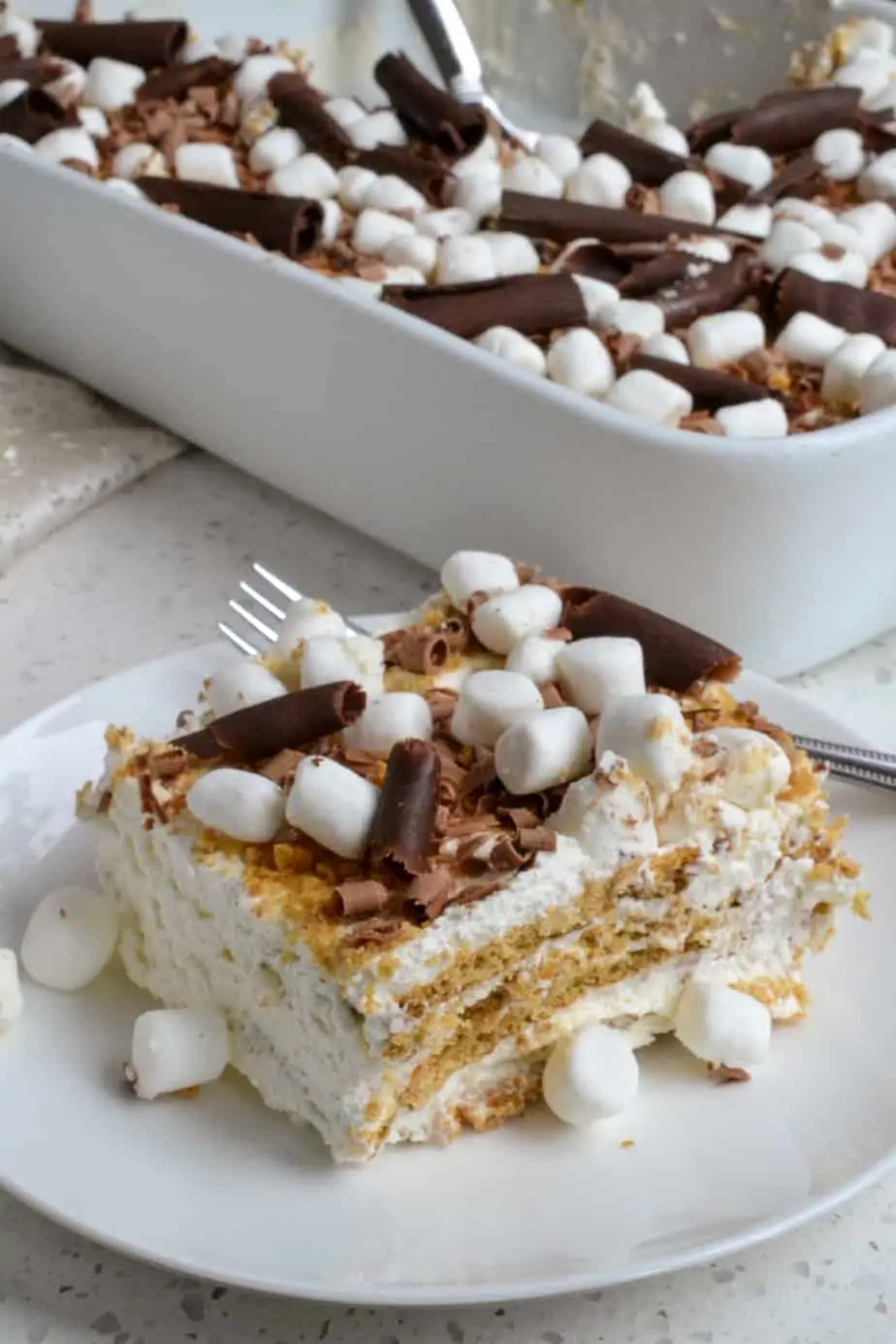 A slice of Icebox Cake topped with crushed graham crackers, mini marshmallows, and chocolate curls. 