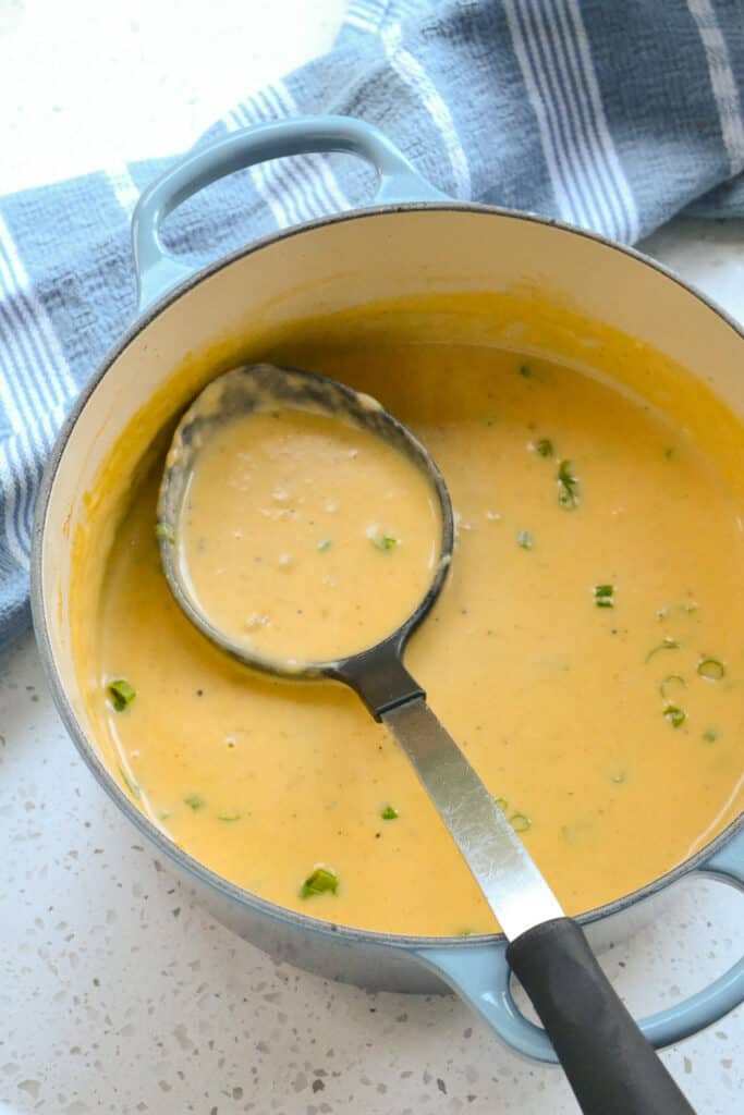 A Dutch Oven full of beer cheese soup topped with thin sliced green onions. 