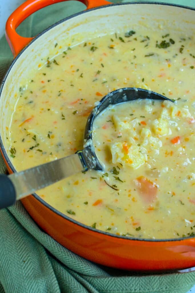 A pot full of cheese cauliflower soup with onion, celery, and carrots. 