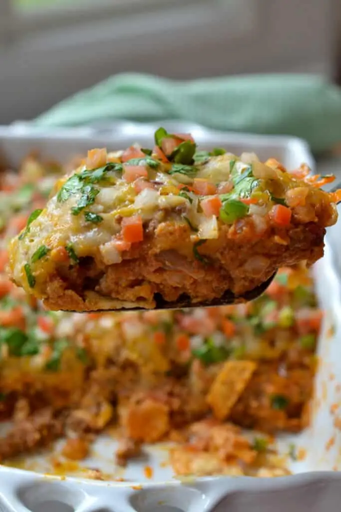 A tasty Taco Casserole made with tortilla chips, refried beans, taco-seasoned ground beef, cheddar,  Monterey Jack Cheese, cilantro, and Pico de Gallo. 