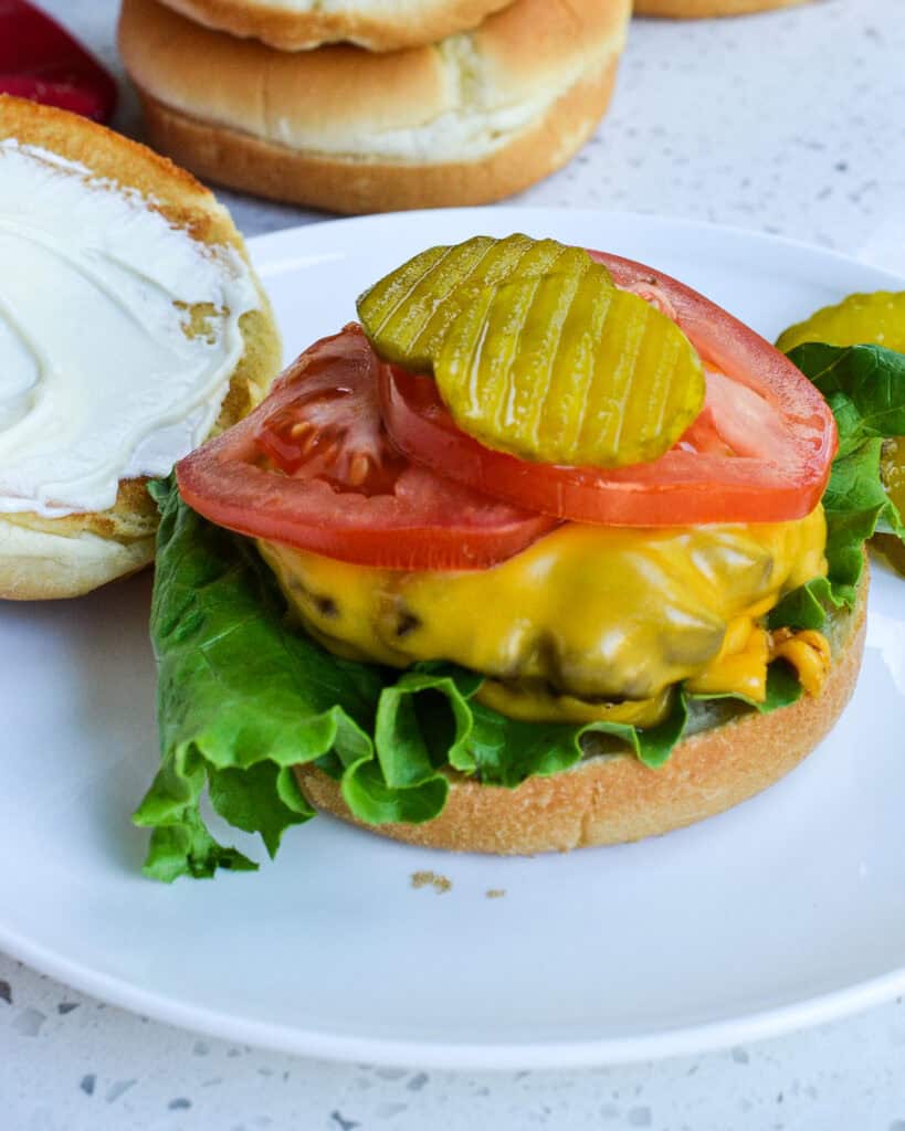 An air fried burger on a bun on a plate with mayo, pickles, and tomatoes. 