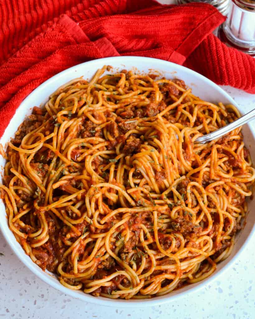 A big bowl up close of Instant Pot Spaghetti with a fork and fresh herbs on top.