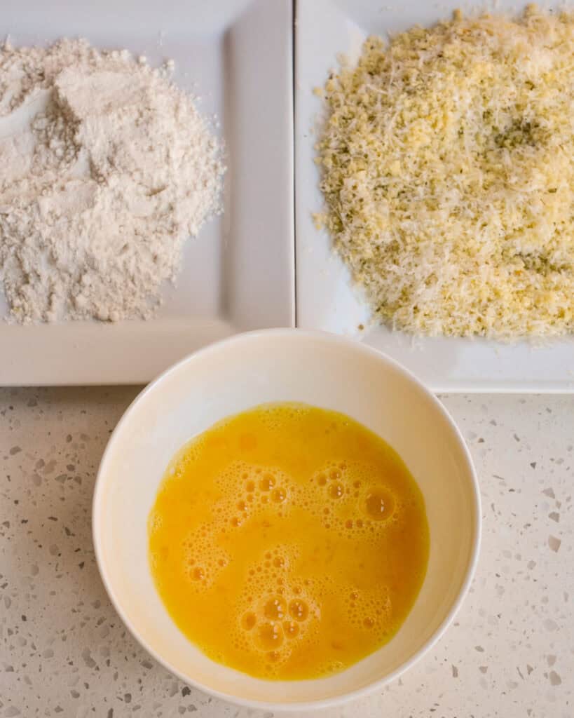Set up two breading stations and a dunking station. Dredge the chicken in flour, dip it in eggs, and coat both sides with the panko-parmesan mixture.