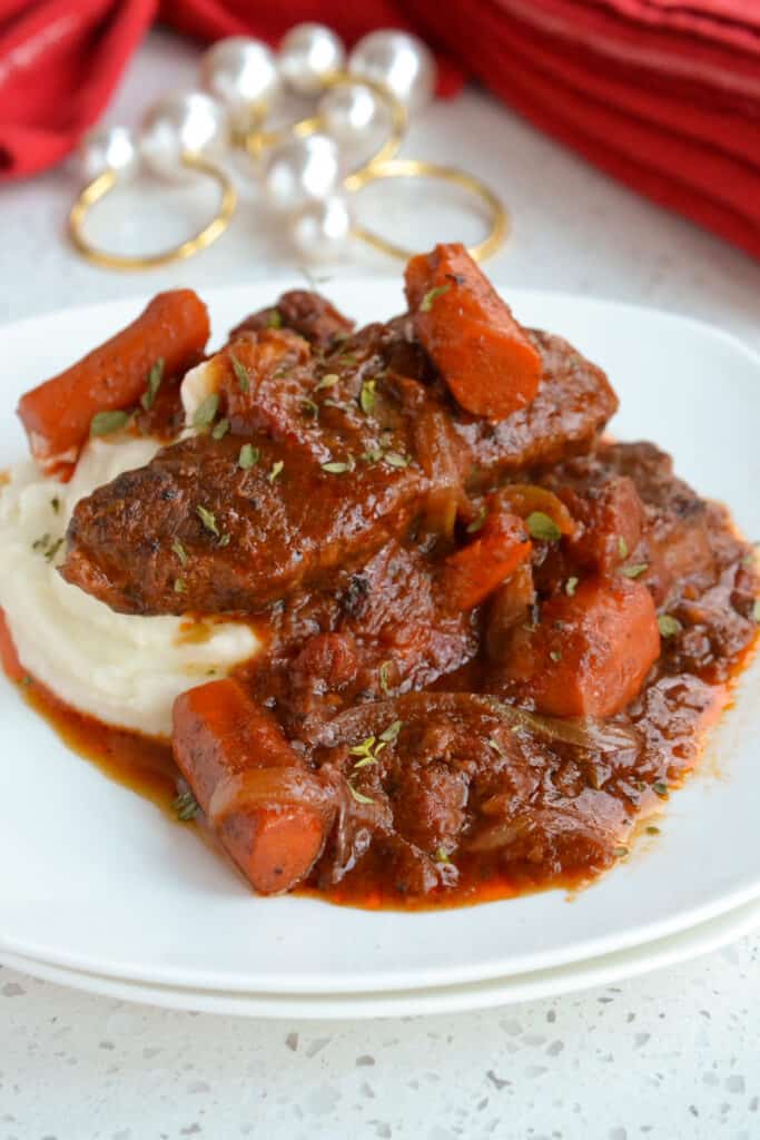 A plate full of swiss steak with a rich tomato gravy ladled over creamy mashed potatoes. 