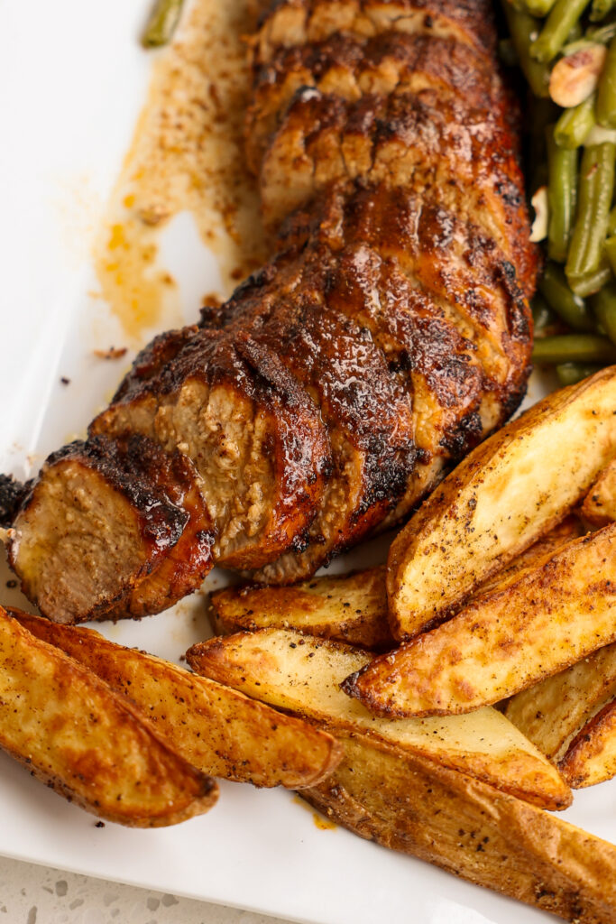 A platter with air fryer pork tenderloin, green beans, and potato wedges. 