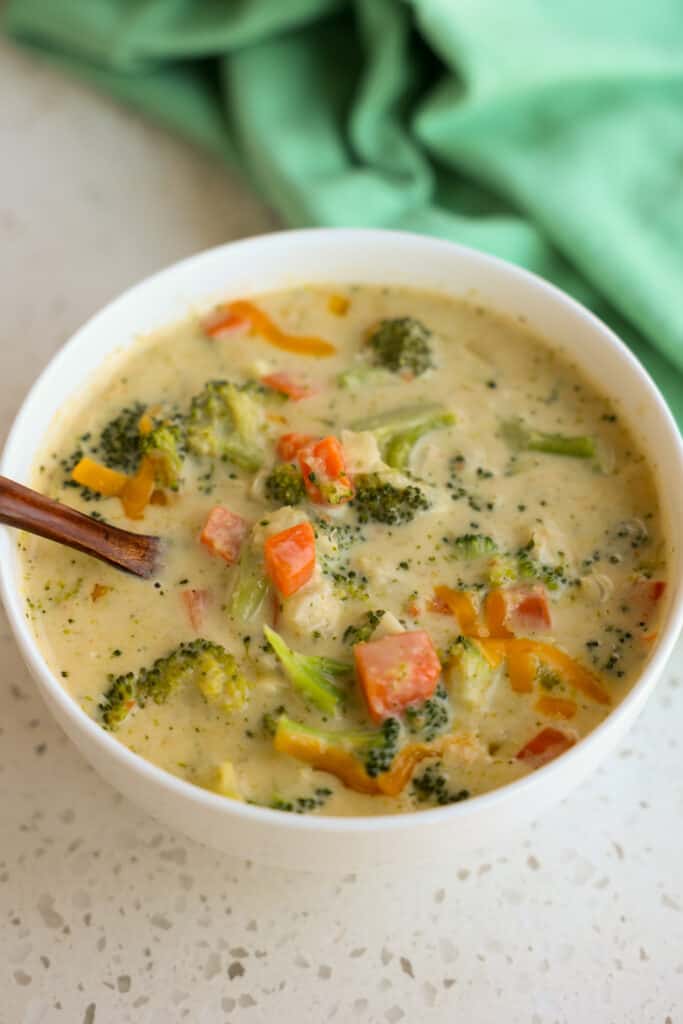 A bowl full of broccoli cheddar soup with onions, carrots, and celery. 