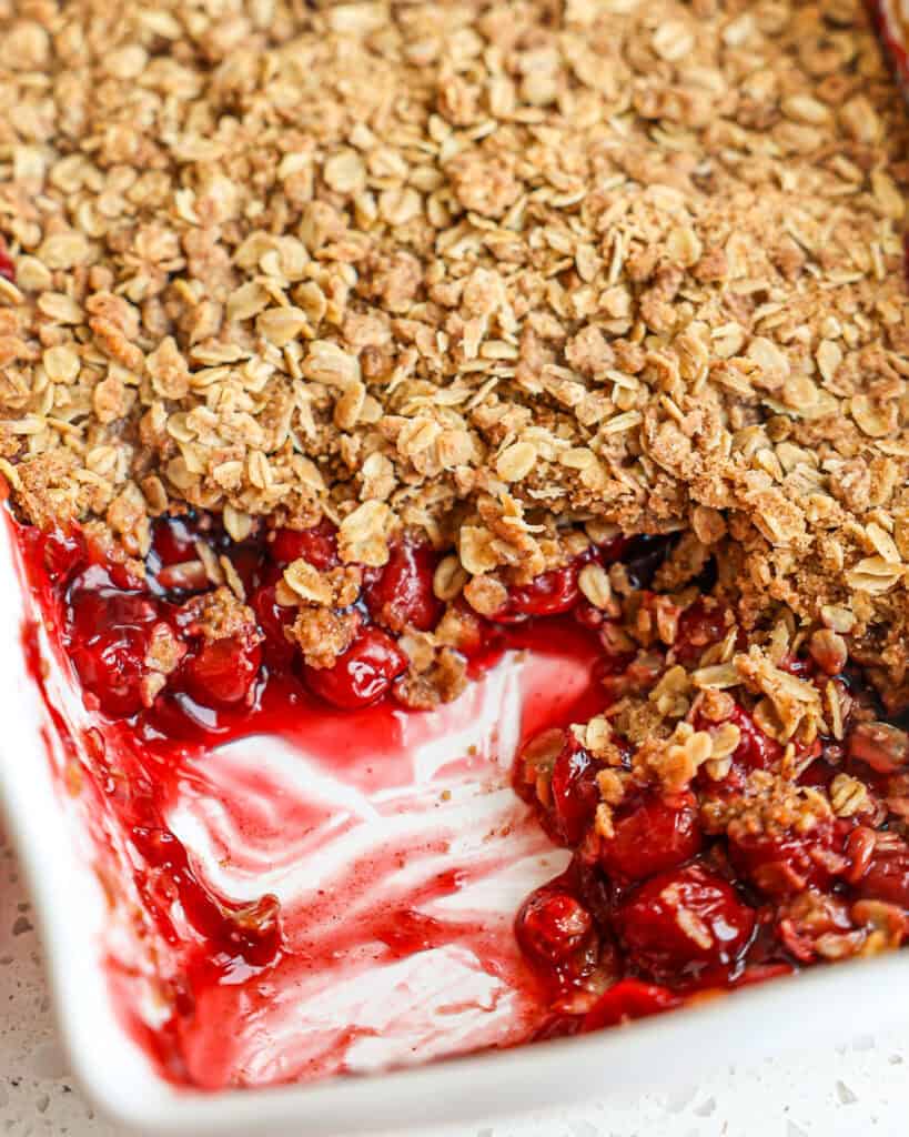A baking full of cherry cobbler with a couple of spoonfuls missing. 
