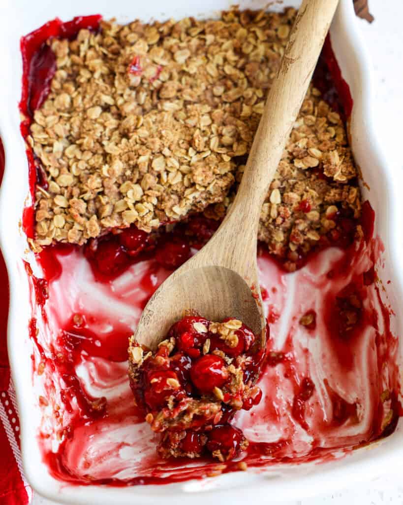A baking dish full of cherry crisp with a wooden spoon in it. 