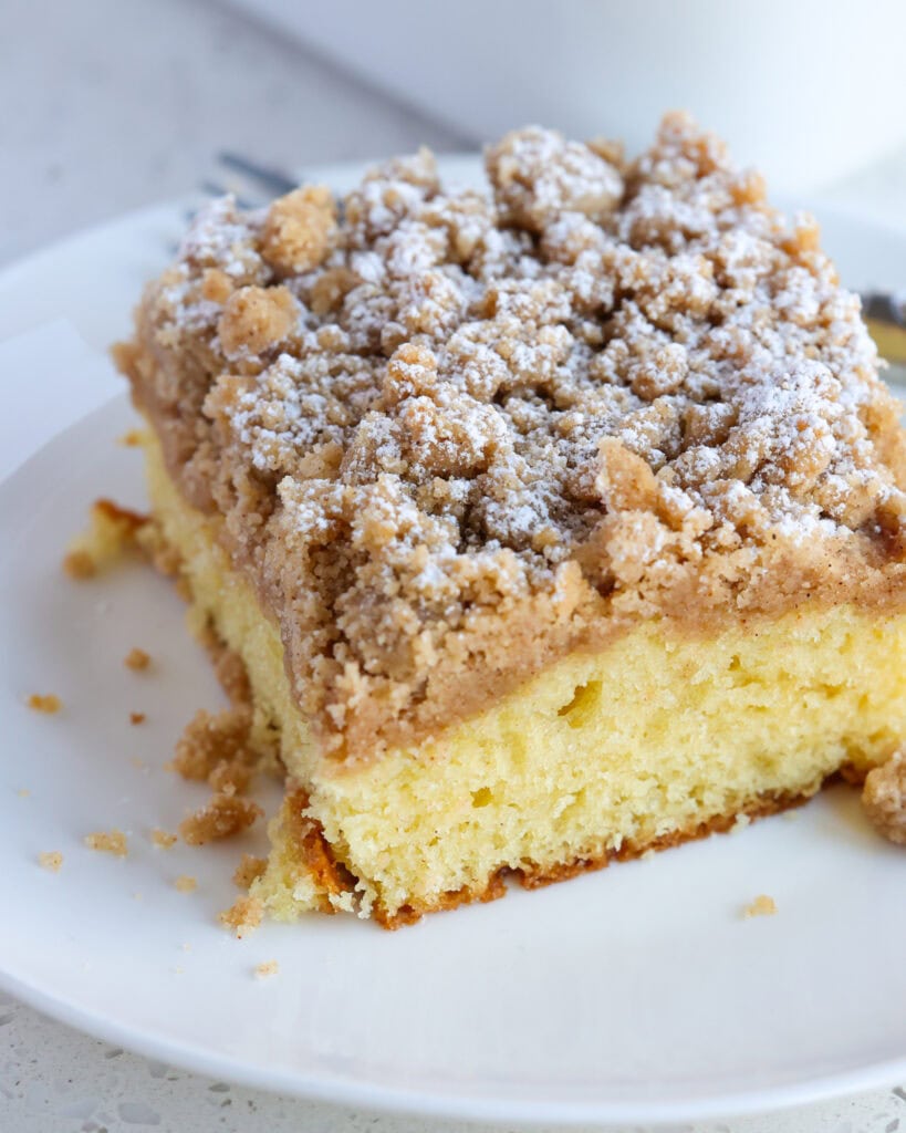 A close up views of cinnamon crumb cake on a white plate with a fork.