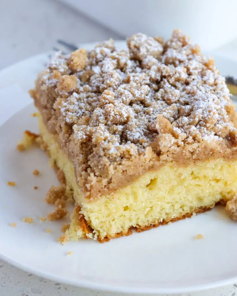 A close up views of cinnamon crumb cake on a white plate with a fork. 