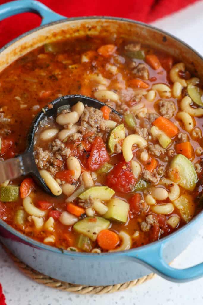 A ladle full of tasty soup with Italian Sausage, onion celery, carrots, zucchini, tomatoes, beans, and pasta. 
